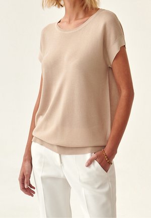 Top beige de manga corta de punto con cuello redondo y corte relajado; combinado con pantalones blancos; textura lisa con sutil acanalado.