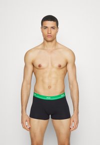 Black boxer briefs with a green waistband featuring "BOSS" branding, made from a smooth, stretchy fabric, offering a snug fit.