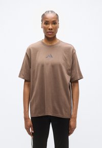 Καφέ βαμβακερό t-shirt με στρογγυλή λαιμόκοψη και άνετη εφαρμογή, με μικρό σκοτεινό λογότυπο στο στήθος και κοντά μανίκια.