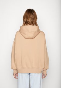 Maundá oversized bege com uma capuz grande, textura suave, ombros caídos e punhos canelados. Usada com calças azul claro.