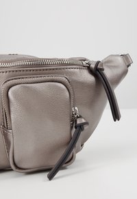 Banane en cuir gris métallisé avec deux compartiments zippés et tirettes en cuir noir.