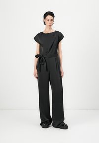 Jardín negro con mangas cortas, escote redondo, cinta en la cintura y pantalones de pierna ancha, hechos de una tela suave y ligera.