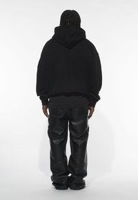Sort oversized hoodie med en stor hætte bagpå, parret med baggy sorte læderbukser. Glat tekstur og minimal detaljering.