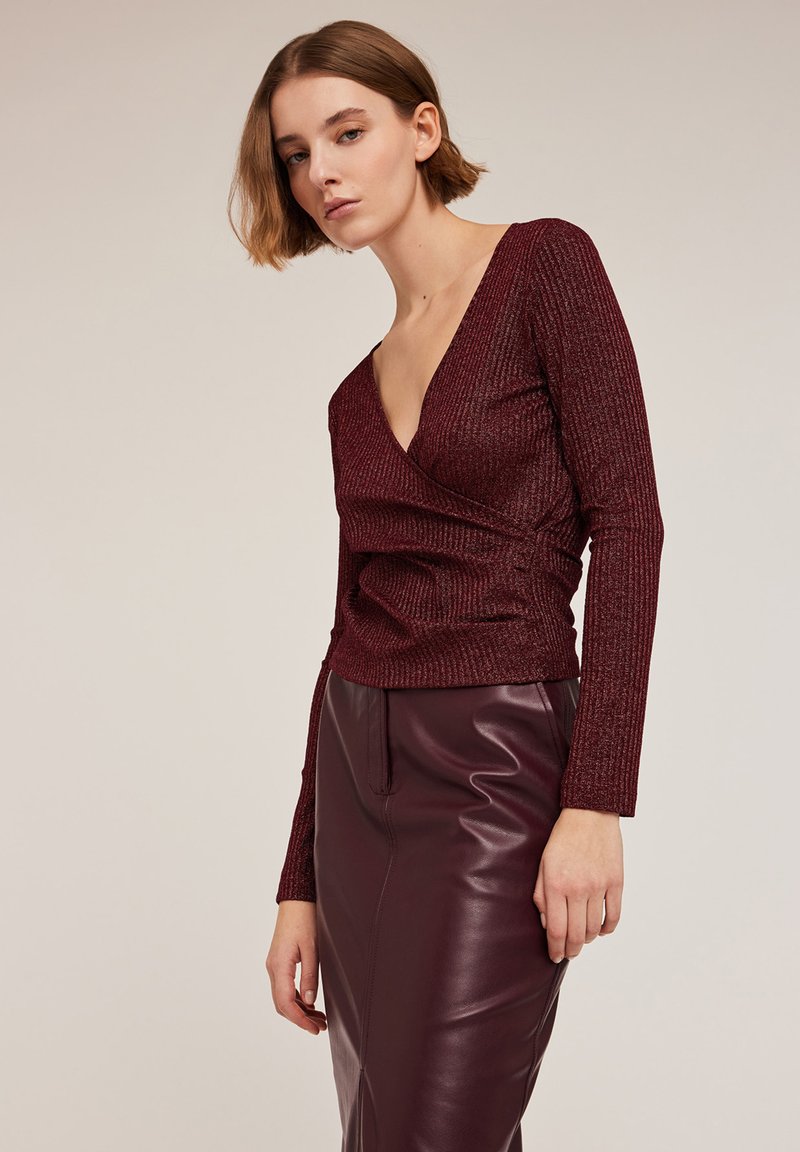 Burgundyröd ribbad långärmad topp med en djup V-ringning och en figurnära silhuett, tillsammans med en matchande hög midja läderkjol.