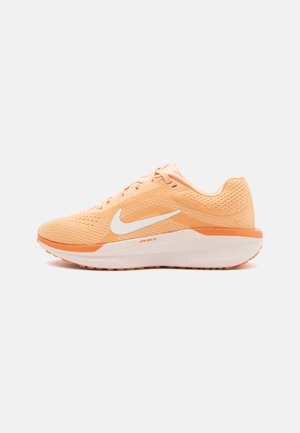 Gaiši oranža sporta apava ar acs augšdaļu, balto Nike swoosh, mīkstinātu balto viduszoli un teksturētu gumijas zoli.