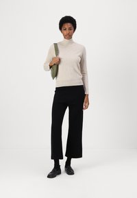 Bež turtleneck pulover, črne široke hlače, čevlji v črni barvi in olivno zeleni torba. Gladka tekstura, minimalističen dizajn.