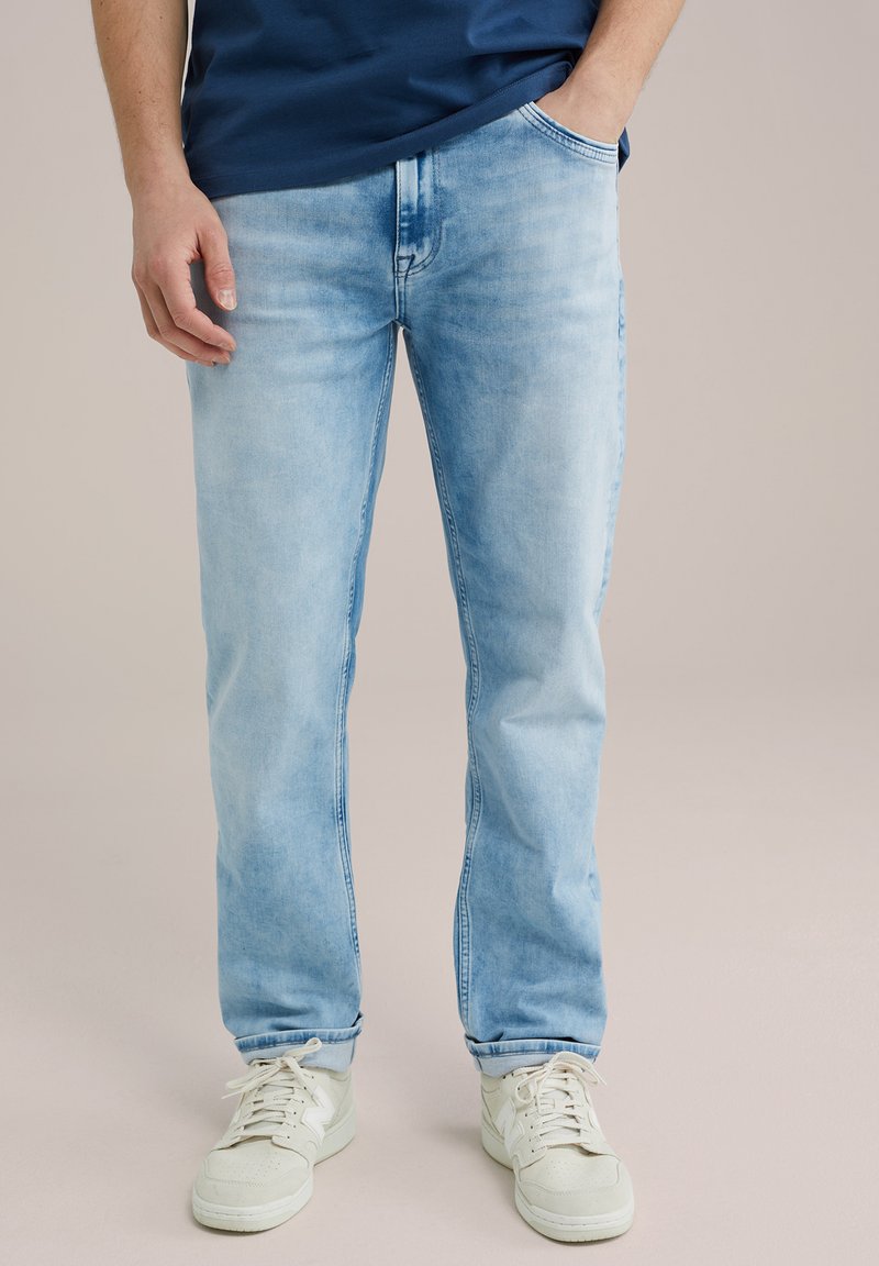 Jeans in denim blu chiaro con taglio dritto, caratterizzati da una finitura sbiadita, cinque tasche e una leggera affusolatura alle caviglie, abbinati a sneakers bianche.