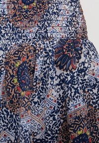 Kankaan hame, jossa on kukka- ja geometrisia kuvioita sinisen, kermanvärisen ja ruskean sävyissä; rypistetty vyötäröyksityiskohta parantaa tekstuuria ja istuvuutta.