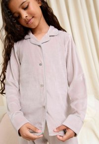 Conjunto de pijama de tela suave y rosa, con mangas largas, botones en la parte delantera y ribetes plateados en el cuello y los puños, presentando un diseño de ajuste relajado.