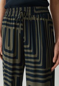 Lichte, gestreepte broek in olijfgroen met marineblauwe abstracte lijnen. Voorzien van een elastische tailleband met een trekkoord voor een verstelbare pasvorm.