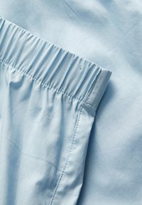 Helles blaufarbenes Gewebe mit sanfter Textur, ausgestattet mit einem elastischen Bund und Nähdetails für eine lockere Passform. Nahaufnahme des Stoffmaterials.