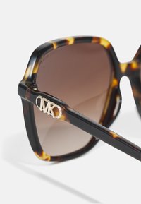 Sunglasses su šarvuota korpusu ir tamsiai ruda gradiento spalvos objektyvais. Brangakmenio logotipas ant šventykloje, pagaminti iš blizgios plastiko medžiagos.