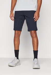Shorts navy avec une poche avant, un ourlet roulé et un matériau léger, associés à des baskets grises et des chaussettes foncées.