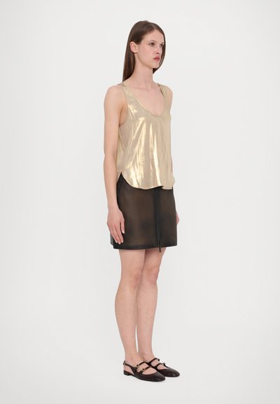 Metallic gold ilmanhihainen toppi syvällä v-neckilla, yhdistetty mustaan nahkaiseen minihelmaan, jossa on etuvetoketju ja sileä pinta.