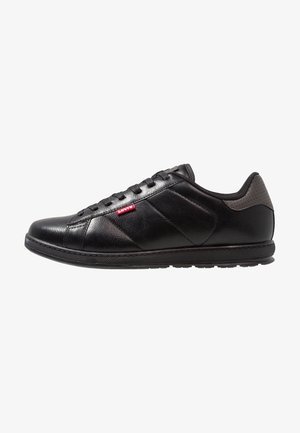 Zapatilla baja de cuero negro con cordones negros, suela texturizada y una pequeña etiqueta roja con el logo de Levi's en el panel lateral.