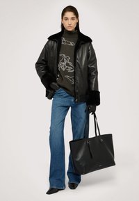 Svart läderjacka med pälskrage, grå tröja med djurdesign, blå utsvängda jeans, svarta handskar och en stor svart tote-väska.