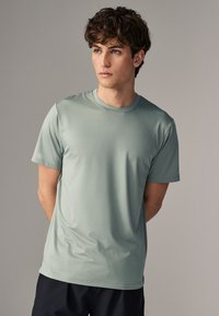 Camiseta deportiva de manga corta, color verde claro, hecha de un tejido texturizado, con un diseño de cuello redondo, combinada con pantalones cortos oscuros.