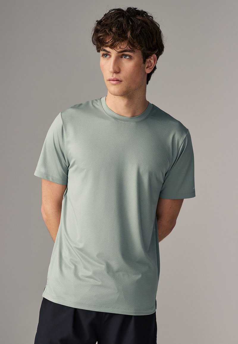 Camiseta deportiva de manga corta, color verde claro, hecha de un tejido texturizado, con un diseño de cuello redondo, combinada con pantalones cortos oscuros.