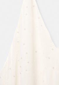 Tablier blanc avec des motifs brodés circulaires subtils, tissu doux, suspendu sur un fond clair uni.