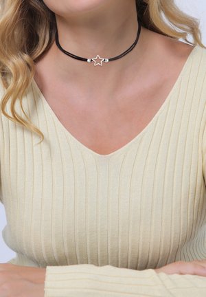 Black choker necklace with a star pendant and metallic accents, worn on a textured beige top with a deep V-neckline.