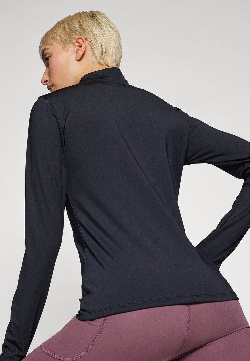 Top nero a maniche lunghe in tessuto elasticizzato, con colletto alto e spalle seamless, abbinato a leggings rosa scuro.