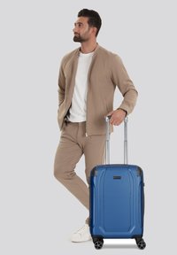 Maleta rígida azul con una superficie texturizada, con un mango telescópico y cuatro ruedas para mayor movilidad.