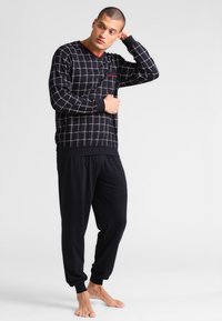 Zwart geruite lange mouwen top met rode accenten en effen zwarte joggingbroek. Zacht materiaal, relaxte pasvorm, met ribgebreide manchetten en tailleband.