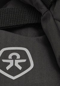 Črn material z herringbone vzorcem, ki vključuje gladek, sijoč sivi logo in trajno spletno naramnico. Povečan detalj materiala.