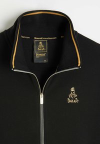 Czarna kurtka na zamek z złotym wykończeniem przy kołnierzu,logo Dakar haftowane na złoto na klatce piersiowej oraz metka w rozmiarze XL wewnątrz kołnierza.