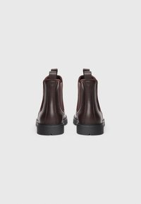 Botas de tobillo de cuero marrón con un acabado suave, paneles laterales elásticos y una suela de goma negra. Dos tiradores en la parte trasera para facilitar el calzado.