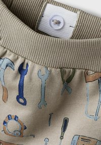 Beiger Stoff mit Abbildungen von Werkzeugen. Gerippter Bund mit weißem Knopfverschluss. Strukturierte Oberfläche mit bunten Druckmotiven.
