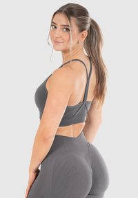 Grijze sportieve crop top met een dubbele bandontwerp en een open rug. De stof is glad en aansluitend, waardoor de lichaamsbouw van de drager wordt benadrukt.