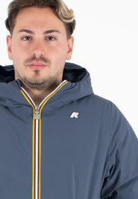 Grijze hoodie met een voorzipper met een metalen trekker, levendige gestreepte accenten en een logo op de borst. Glad textuur.
