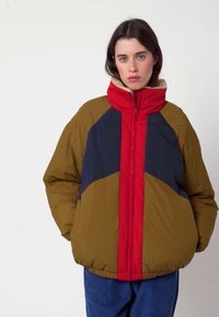 Steppjacke in Olivgrün, Marineblau und Rot. Mit hohem Kragen, Reißverschluss und kontrastierendem Farbblock-Design. Weiche Textur.