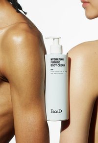 Flacone bianco di "Crema per il Corpo Idratante e Tonnificante" con testo nero, posizionato su una spalla nuda che mostra una texture liscia e lucida.