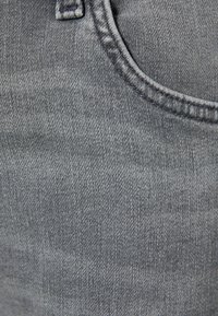 Acercamiento de una tela de mezclilla negra descolorida con costuras visibles alrededor del borde de un bolsillo.