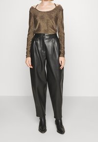 Langärmliges, schulterfreies Oberteil aus bronzefarbenem Glitzer, kombiniert mit hoch geschnittenen, schwarzen Hosen aus Kunstleder und schwarzen Ankle Boots.