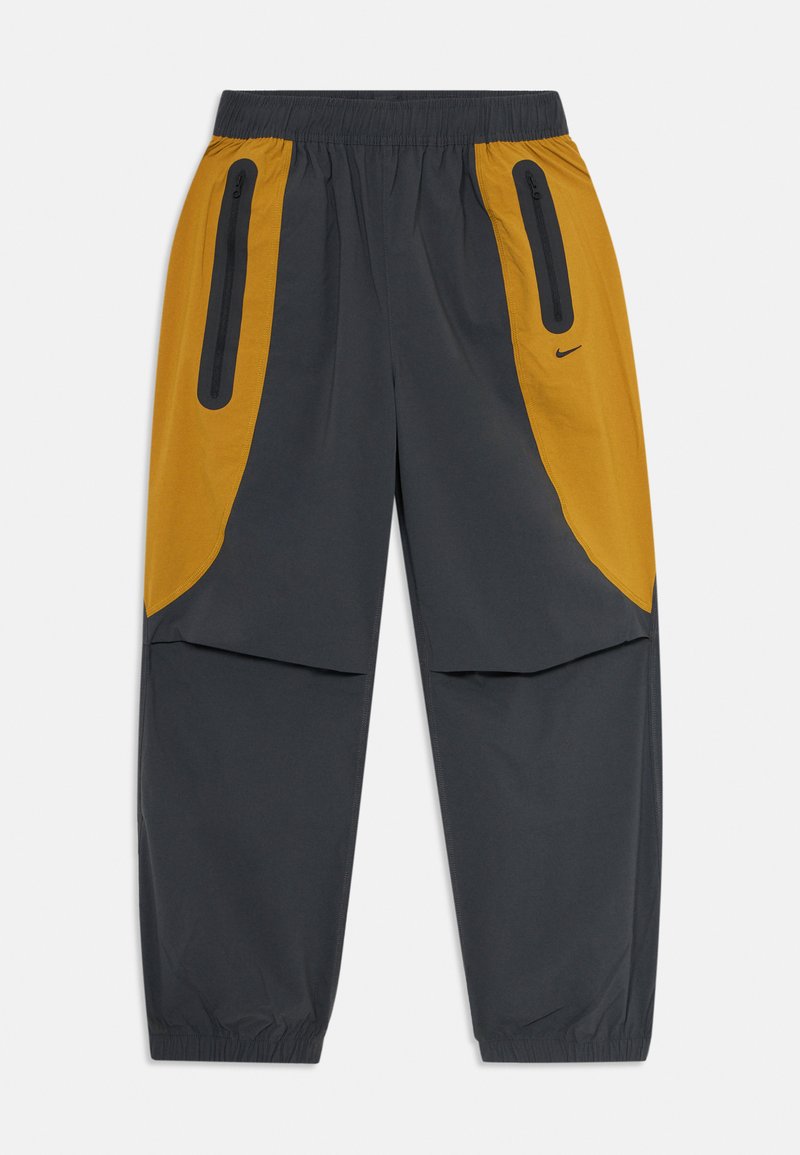 Vīriešu melnā un sinepju dzeltenā neilona sporta bikses ar elastīgu jostu un piedurknēm, vertikālām rāvējslēdzēju kabatām un mazu melnu Nike swoosh logo labajā pusē.