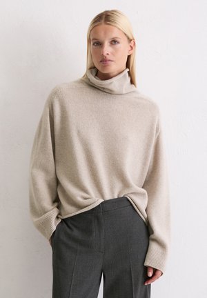 Beige coltrui gemaakt van zacht breiwerk, met lange mouwen en een relaxte pasvorm, gecombineerd met donkergrijze geruite broek.