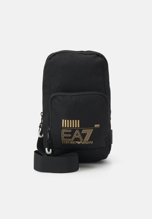 Bolsa cruzada de tela negra con el logo dorado de EA7 Emporio Armani, que cuenta con un bolsillo frontal y una correa ajustable. Textura suave, forma rectangular.