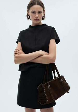 Borsa in suede marrone con dettagli arricciati sui lati, hardware in argento e doppie cinghie per spalla. Il modello indossa una maglietta nera e una gonna.