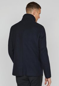 Chaqueta de mezcla de lana en color marino que presenta un cuello alto, hombros estructurados y una superficie suave y texturada; diseñada con un ajuste entallado.