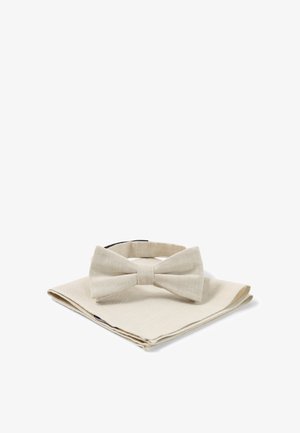 Beżowa muszka z tkaniny spoczywająca na dopasowanej beżowej serwetce, obie na białym tle.