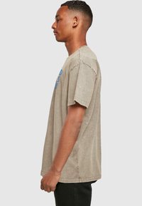 Beige bomulds t-shirt med afslappet pasform. Har blå tekst på forsiden, korte ærmer og rund halsudskæring. Glat tekstur.