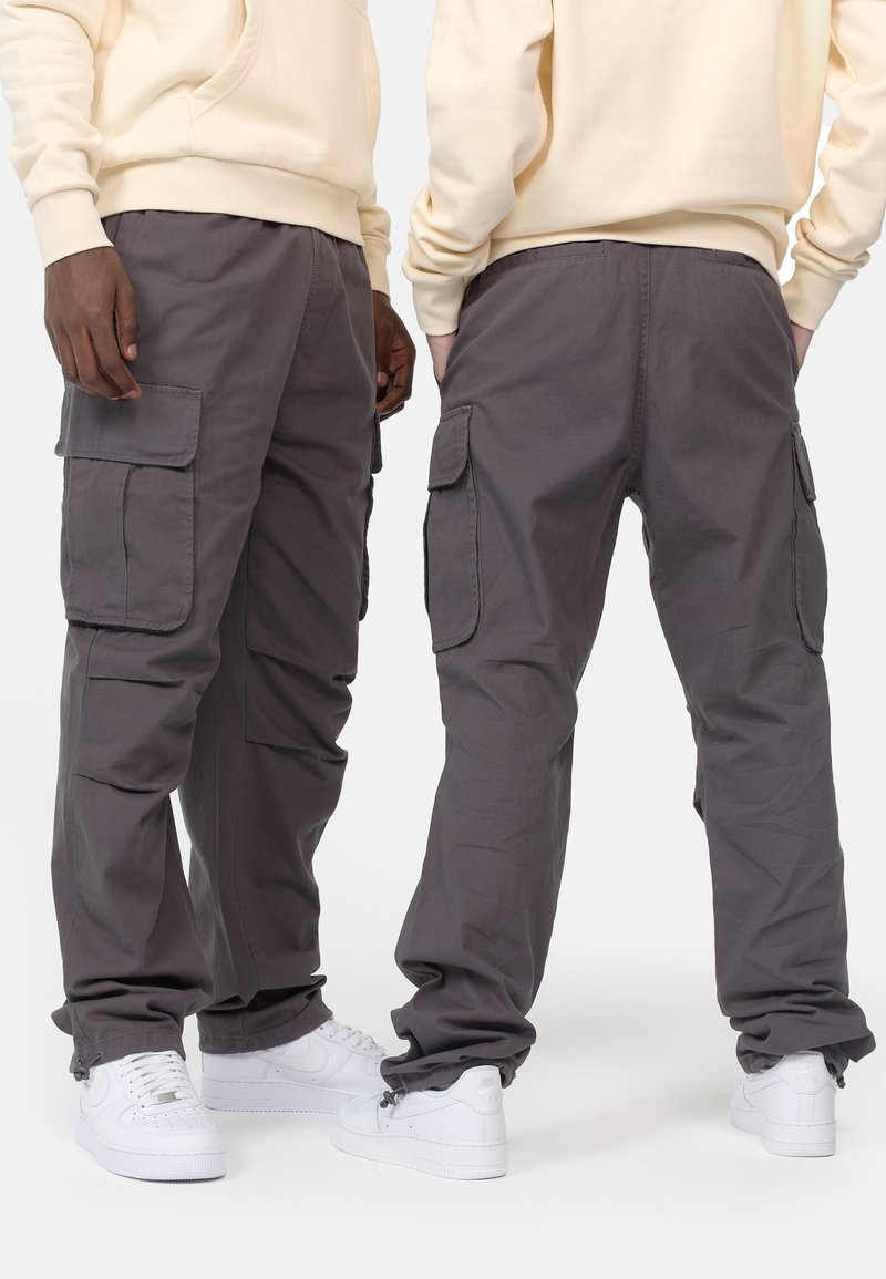 Deux personnes portant un pantalon cargo gris avec des poches latérales et des baskets blanches, vues de face et de dos.