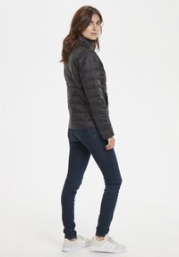 Svart puffjacka med hög krage, vadderad design och slim fit, kombinerad med mörka skinny jeans och vita sneakers.