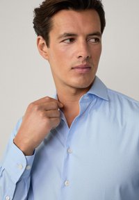 Light blue striped dress shirt with a spread collar, white buttons, and long sleeves. Fabric appears smooth with a fine texture.