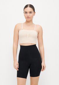 Nude crop top with thin straps and gathered front detail, paired with high-waisted black shorts, both fitted and smooth-textured.