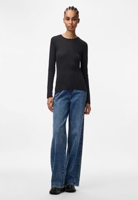 Must musternääriga must särk, millel on pikad varrukad ja laiad, kõrge vöökohaga sinised teksad. Särgil on ümmargune kaelus ja pehme tekstuur. Väljanägemise täiendavad juhuslikud jalatsid.