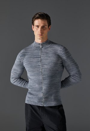 Haut zippé gris à manches longues, texturé, fabriqué à partir d'un tissu à motif en grille, avec un col montant et une coupe ajustée.